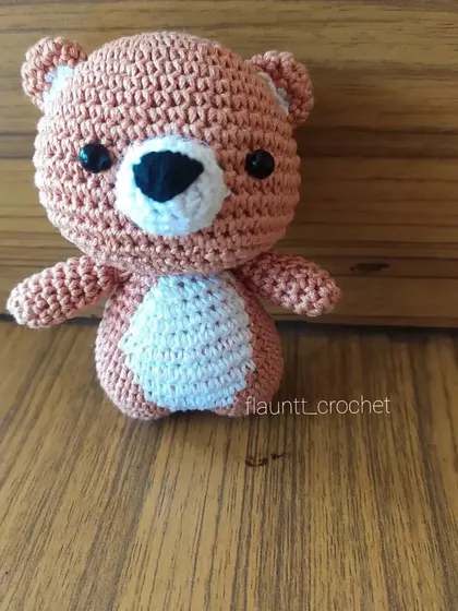 A single teddy bear charm sitting on a wooden surface. The warm brown color and white belly patch make it a classic design that everyone loves.