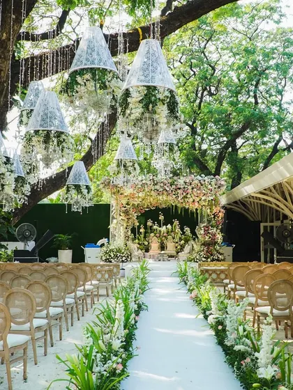 The wedding aisle, lined with lush greenery and with floral chandeliers hanging from the trees, created an enchanted garden path leading to a fairytale mandap.