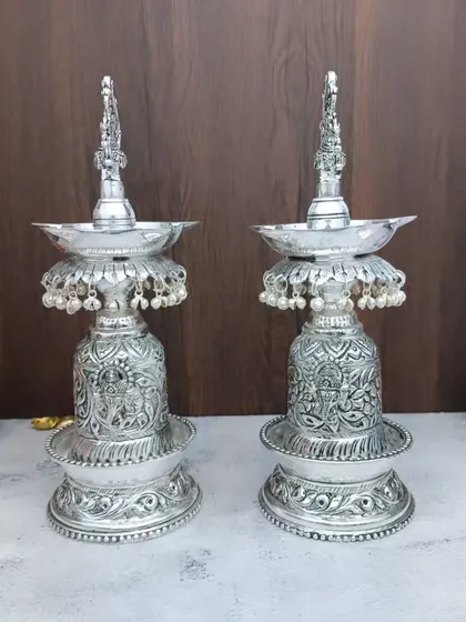 German silver se bane yeh Hamsa designer diya ka joda aapke pooja ghar ki shobha badha dega. Inka antique finish aur neeche lage moti inhein ek royal look dete hain.