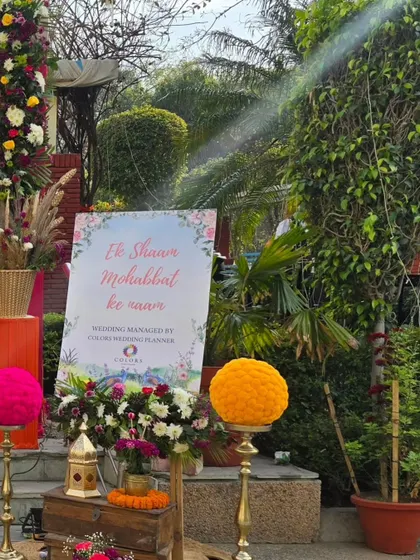 Another angle of the 'Ek Shaam Mohabbat ke naam' welcome sign, showing how it's integrated into the overall entrance decor with large marigold spheres and rustic wooden crates.
