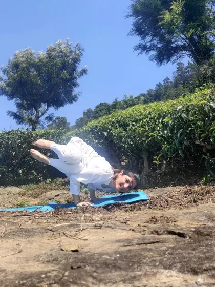 Arm balance on a mat among tea bushes, a Yoga Day practice taken outdoors.