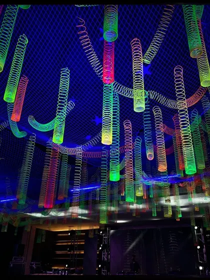 A detailed shot looking up at the ceiling installation of colorful, glowing slinky toys. The arrangement was designed to look like a cascade of light and color, adding a playful element to the corporate event.