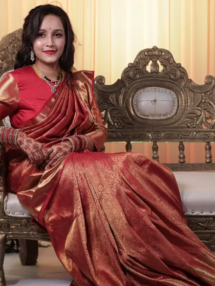 Vaibhavi seated, looking like royalty. The rich red of her saree and lips creates a powerful and elegant statement for her evening event.