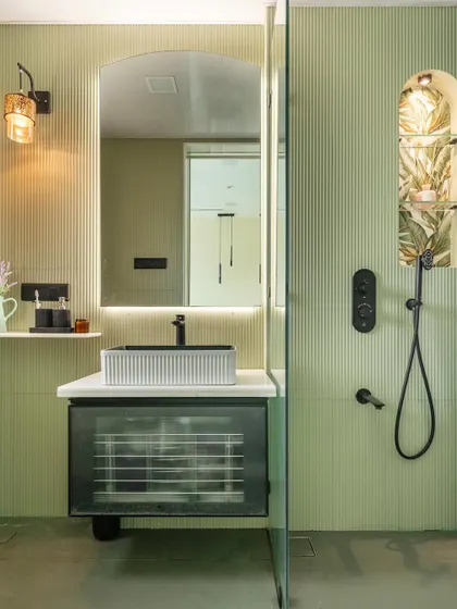 This master bathroom is a serene oasis, featuring soft green fluted walls and a unique shower niche with botanical wallpaper. The floating vanity with a reeded glass front and the modern black fixtures add a touch of contemporary elegance.