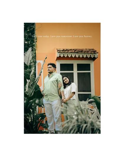A romantic portrait of a couple standing in front of a house, framed by lush greenery.