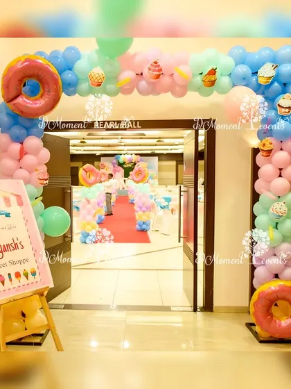 A delightful entrance to "Aayansh's Sweet Shoppe," with a balloon arch decorated with donut and cupcake details and a charming welcome sign.