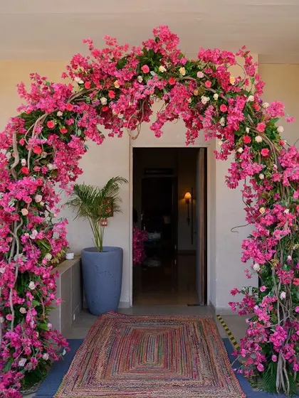 A dreamy entrance arch for a mehendi, completely covered in vibrant pink bougainvillea and roses.