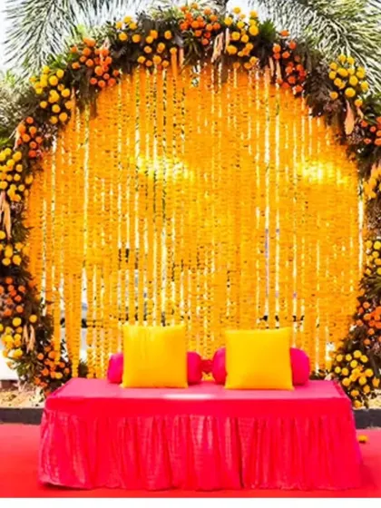 Our most requested Haldi backdrop design. A large ring of marigolds frames a curtain of genda strings, with a simple diwan for seating, perfect for any outdoor pre-wedding event.
