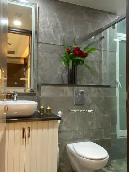 A compact and elegant bathroom design. The space features grey marble-finish tiles, a vessel sink on a white vanity, and a simple glass partition for the shower area.