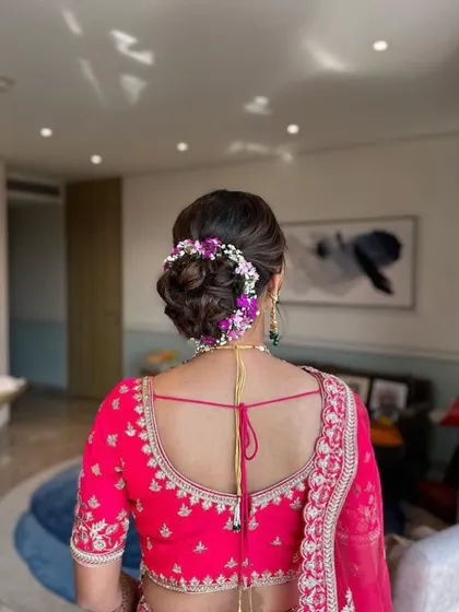 This beautiful floral bun is created with a mix of purple and white flowers to match the bride's pink lehenga. It's a soft, romantic updo perfect for a wedding ceremony.