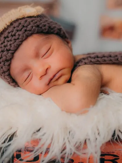 A close portrait focusing on the baby's sweet face and the texture of the knitted hat. The soft lighting creates a gentle and dreamy mood perfect for newborn photos.