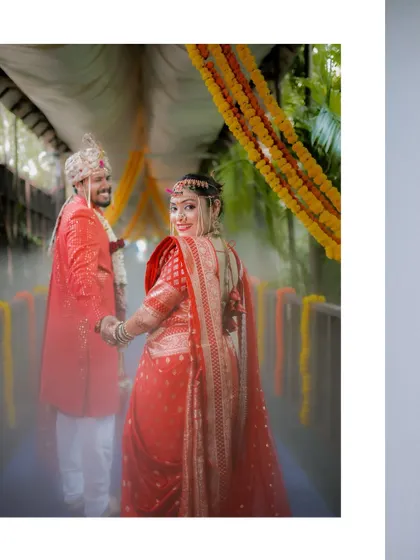 A stunning back-shot of the bride looking over her shoulder as she holds the groom's hand, her red saree's train flowing beautifully.