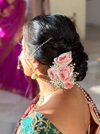 A classic low bun adorned with fresh pink roses and a delicate pearl nath-to-hair chain. This hairstyle is the epitome of grace and is perfect for a traditional wedding ceremony.