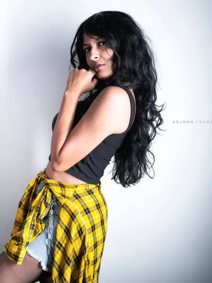 A candid-style shot from the 'Raw Rebellion' series. The pose and styling, featuring a flannel shirt tied at the waist, create an authentic and effortless street-style look.