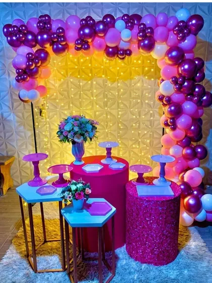 I provide a variety of pedestals and stands to create a multi-level dessert station. This setup in shades of pink is framed by a balloon arch and set against a 3D textured wall.