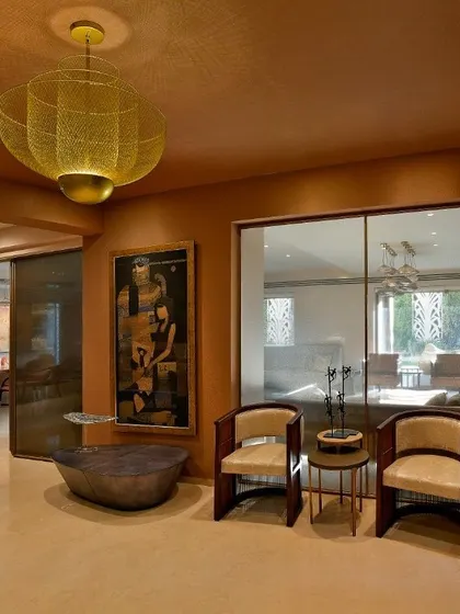 A cozy seating nook in a renovated home, defined by a warm, earthy color palette and a striking brass pendant light. Glass partitions maintain a sense of openness while creating distinct zones for different activities.