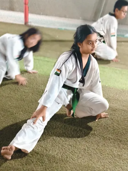 A green belt student holds a side lunge stretch. Her focus and form show the discipline we teach in every aspect of training.