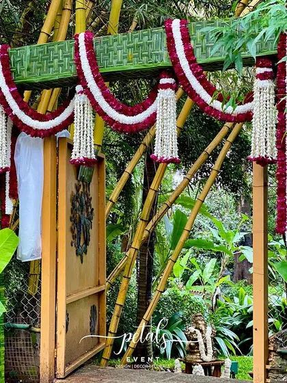 A traditional wedding entrance arch made from woven coconut leaves and decorated with garlands of maroon and white chrysanthemums. This eco-friendly design is both beautiful and culturally significant.