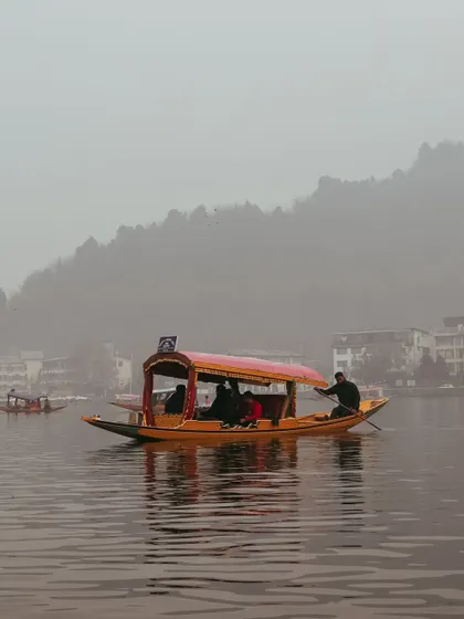 A tourist shikara glides across the misty waters of Dal Lake, filled with people enjoying the peaceful ride.