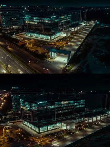 A cinematic aerial perspective of a corporate campus at night, showing the main building, entrance, and parking area illuminated against the dark sky.