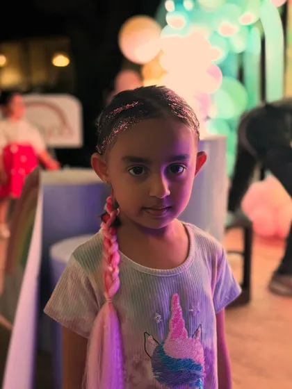 A young girl showing off her unicorn-themed look, with glittery hair and a temporary pink braid to match her shirt.