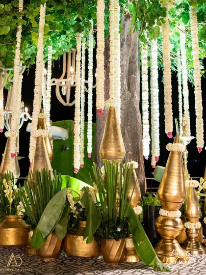 Bold and beautiful decor elements, featuring large golden vases with banana leaves and traditional floral strings hanging from above.