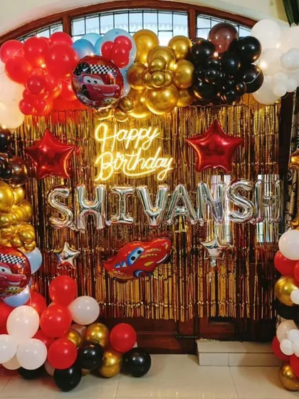 A high-energy Disney Cars theme for Shivansh's first birthday. The decor features a red, black, and gold color scheme, a 'Happy Birthday' neon sign, and foil balloons of Lightning McQueen.