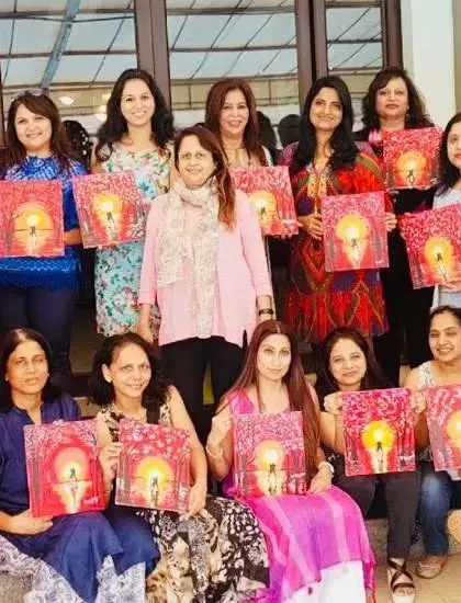 A large group of women celebrating together, each holding their unique painting of a diya. An art party is a wonderful way to mark a special occasion or festival.