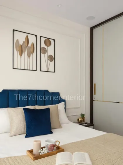 The master bedroom from 'The Adobe' project, featuring a soothing color palette. The royal blue headboard is set against a wall with moulding and framed metal art pieces, uplifting the tranquil aesthetic.