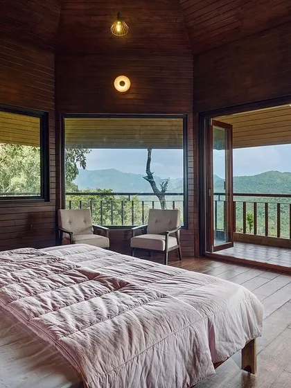 This bedroom opens onto a private balcony with panoramic views of the hills. The use of wood paneling on the walls and floor creates a cozy, cabin-like feel, perfect for a mountain retreat.