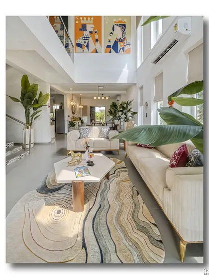 A vertical composition of the double-height living area at Casa D Umravi in Goa. The shot emphasizes the room's scale, from the swirling patterns of the rug on the floor to the vibrant artwork that draws the eye upwards.