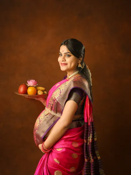 Preserving the glow of motherhood with a traditional touch. This beautiful mom-to-be in a pink silk saree holds a plate of offerings, creating a portrait that is both spiritual and elegant.