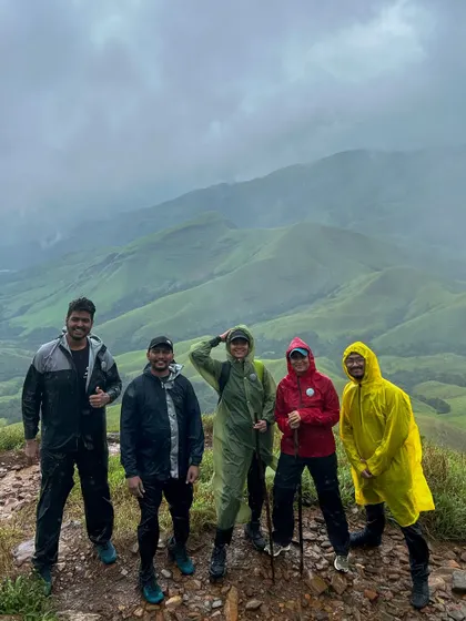 A small group of friends posing at a viewpoint on the Kudremukha trek, their colorful raincoats standing out against the misty green hills.