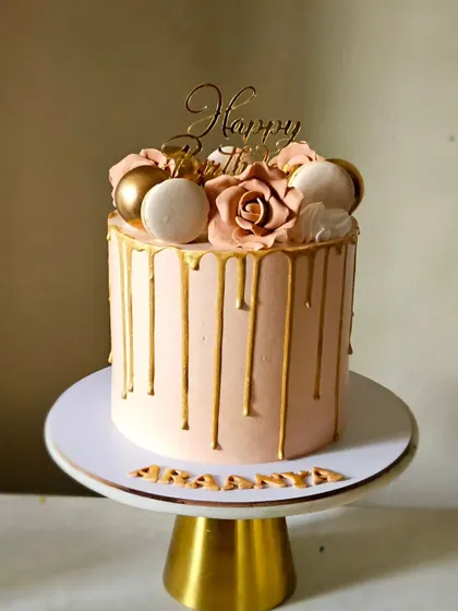 A beautiful monochrome drip cake in a lovely peach tone. The cake is elegantly decorated with a golden drip, handmade sugar roses, and macarons.