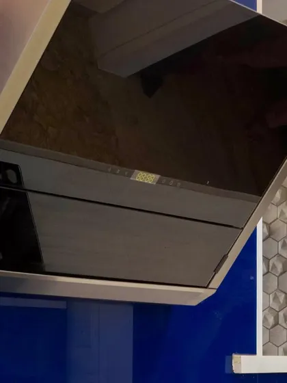 A close-up on a modern, angled chimney hood. The sleek black glass finish complements the bold blue cabinetry in this contemporary kitchen design.
