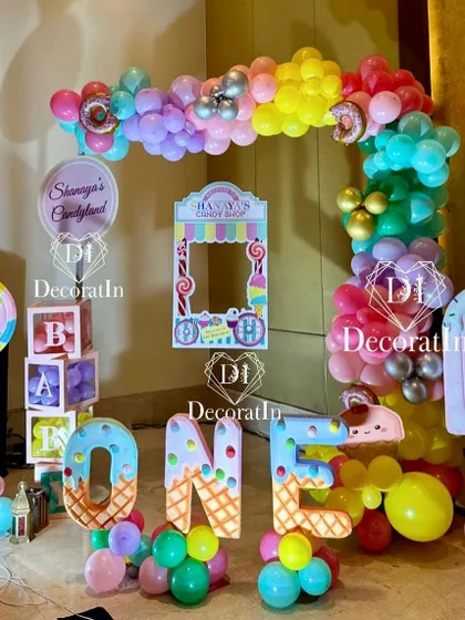 It's so sweet to be one. This vibrant Candyland-themed photo booth is packed with fun, featuring a colorful balloon arch, giant candy props, and a personalized frame for guests to capture sweet moments.