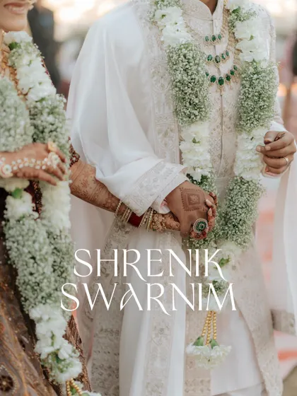 A close-up of the couple holding hands after the Varmala, focusing on the intricate details of their outfits and the floral garlands.