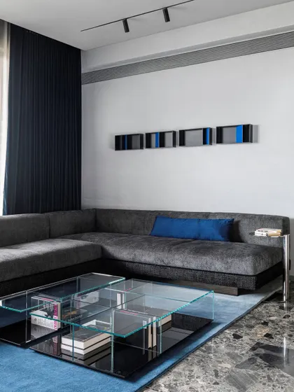 A close-up of the layered glass coffee table and custom sofa, with a hint of blue in the art and cushions.