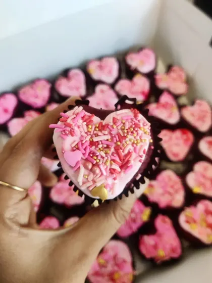A close-up of our heart-shaped red velvet mini cupcake, covered in pink and gold sprinkles. It's a small bite of love.
