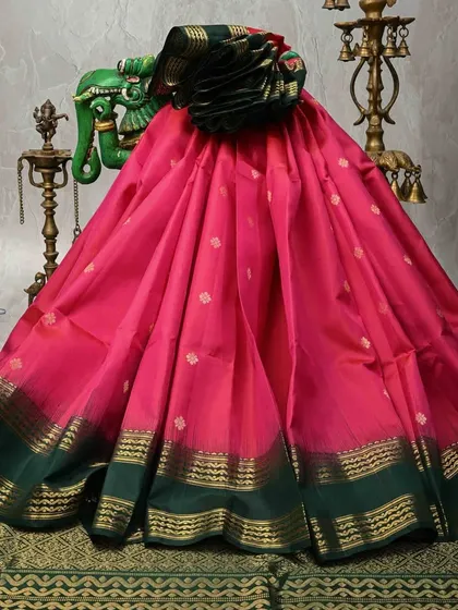 A vibrant pink Kanjivaram with a contrasting dark green border. The small gold butis scattered across the body add a delicate sparkle to this traditional saree.