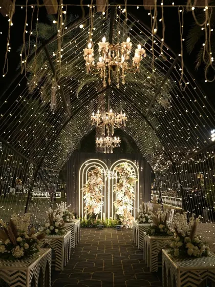 This is how I turn a sangeet night into a celestial dream. A grand tunnel entrance adorned with thousands of fairy lights and elegant chandeliers guides guests into a starry night themed celebration, promising an evening of wonder.