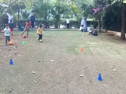 A wide shot of an outdoor football session in a park. We use cones to create different stations and drills, ensuring a structured and varied training experience for the children.