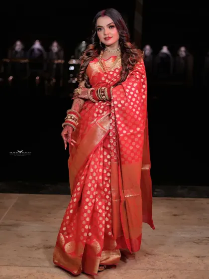 A full-length shot of a woman in a classic red Banarasi saree, perfect for a Karwa Chauth celebration. The dark background makes the vibrant red and gold of the saree stand out.