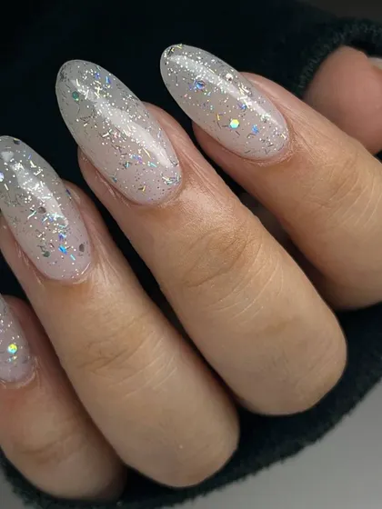 A beautiful, iridescent glitter manicure on long, almond-shaped nails. The multi-colored glitter particles create a magical, unicorn-like effect.
