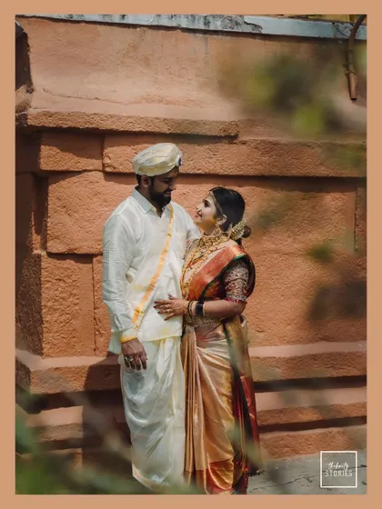 A beautifully composed shot of the couple sharing a quiet moment against a traditional stone wall. This portrait highlights their connection and the timeless aesthetic of their South Indian wedding.