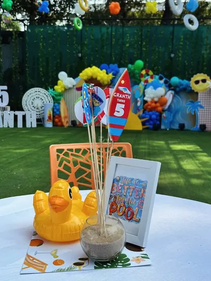 A cute pool-themed centerpiece with a rubber ducky, sand, and a sign that says 'Life is better in the pool'.