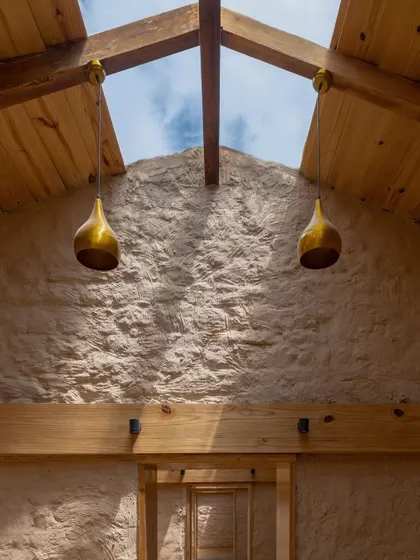 A view looking up towards the skylight, highlighting the contrast between the rough, earthy mud plaster and the clean lines of the wooden roof structure.