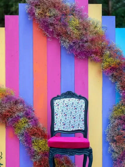 A quirky and colorful photo-op chair, framed by an arc of rainbow-colored baby's breath, perfect for guest pictures.