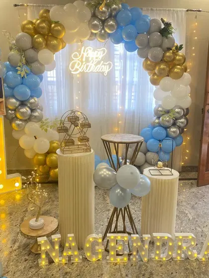 A first birthday party with a circular balloon arch in blue, silver, and gold, a large marquee number "1", and marquee letters.