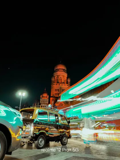 A dynamic night scene in Mumbai, capturing the iconic black and yellow taxi amidst colorful light trails from passing traffic.